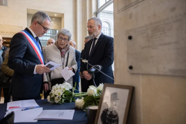Cérémonie commémorative à Dreyfus dans une salle civique française avec plusieurs participants anonymes et fleurs blanches