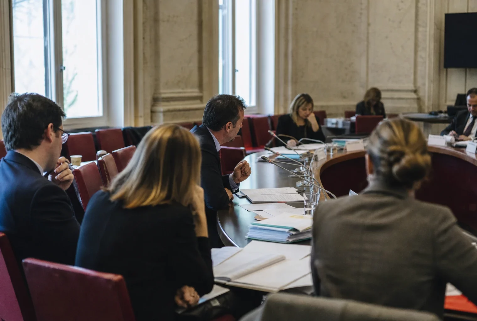 Réunion de commission parlementaire avec micros, dossiers ouverts et élus anonymes dans une salle lumineuse.