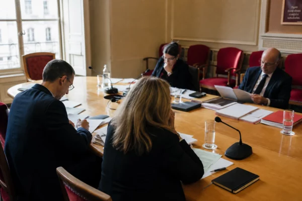 Réunion parlementaire française sur la défense dans une salle de commission, avec micros, dossiers et plusieurs silhouettes anonymes.