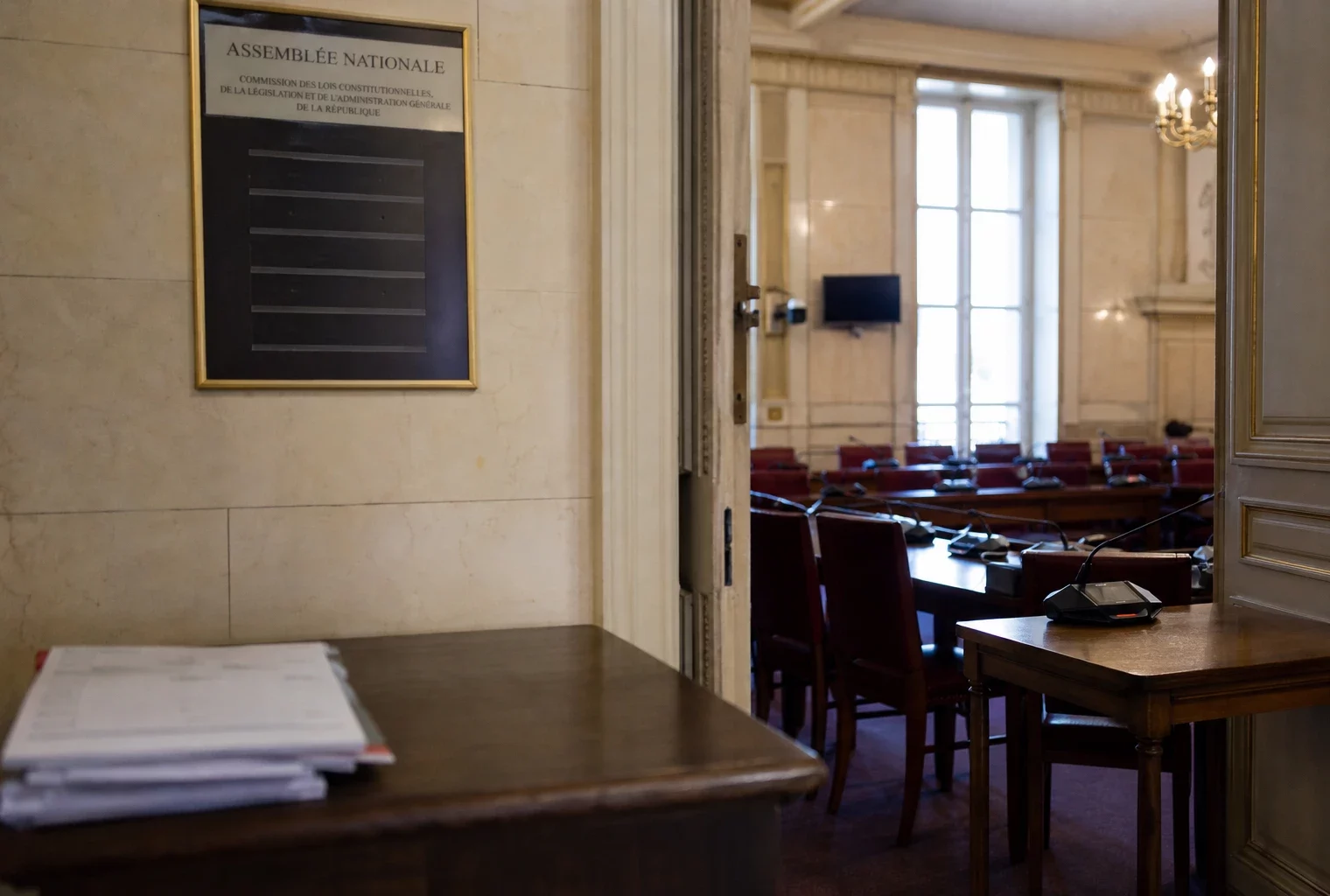 Couloir de l’Assemblée nationale menant à une commission des lois, avec fauteuils rouges et lumière naturelle claire.
