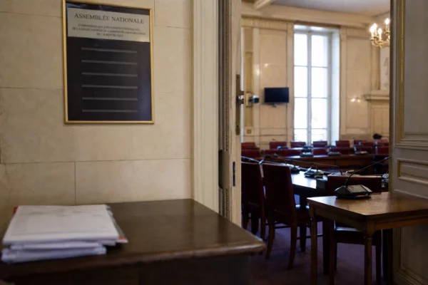 Couloir de l’Assemblée nationale menant à une commission des lois, avec fauteuils rouges et lumière naturelle claire.