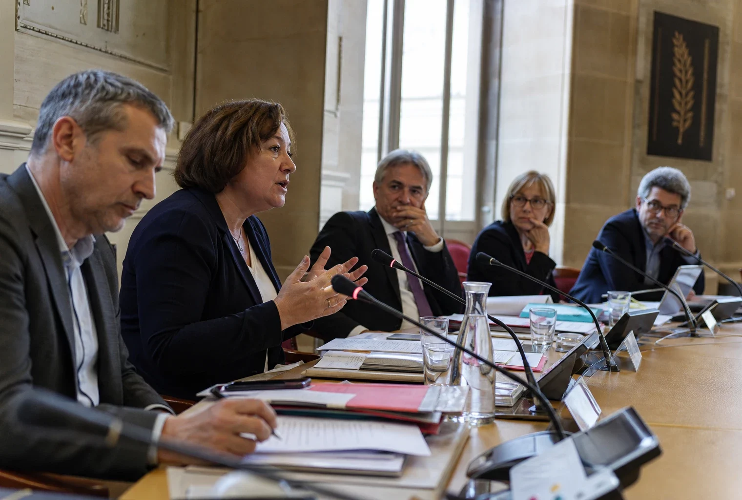 Réunion parlementaire française avec plusieurs élus anonymes, micros et dossiers, dans une salle claire et institutionnelle.
