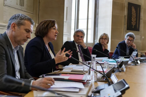 Réunion parlementaire française avec plusieurs élus anonymes, micros et dossiers, dans une salle claire et institutionnelle.