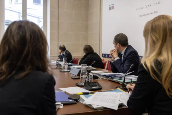 Réunion de commission parlementaire avec micros, dossiers et silhouettes anonymes dans une salle claire