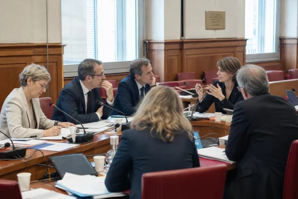 Réunion parlementaire dans une commission, avec micros, dossiers ouverts et plusieurs personnes anonymes en discussion