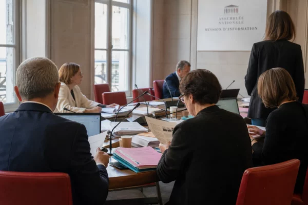 Réunion de commission parlementaire en France avec micros, dossiers et silhouettes anonymes dans une lumière claire.