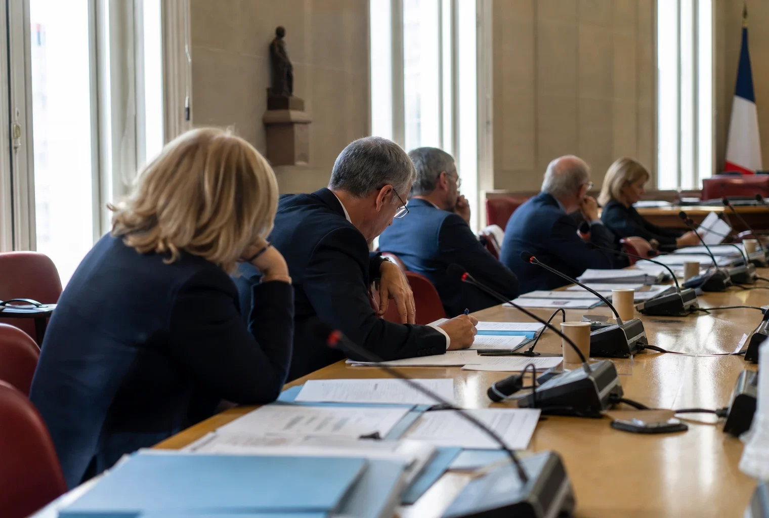 Réunion parlementaire française en commission, avec micros, dossiers et silhouettes anonymes dans une salle lumineuse.