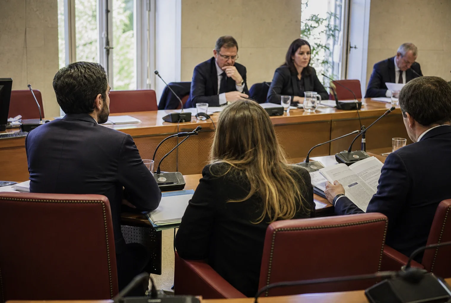 Réunion de commission parlementaire en France avec micros, dossiers et silhouettes anonymes autour d’une table