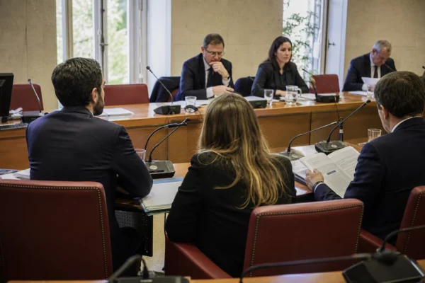 Réunion de commission parlementaire en France avec micros, dossiers et silhouettes anonymes autour d’une table