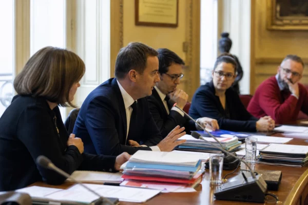 Réunion parlementaire en France avec micros, dossiers ouverts et silhouettes anonymes autour d’une table