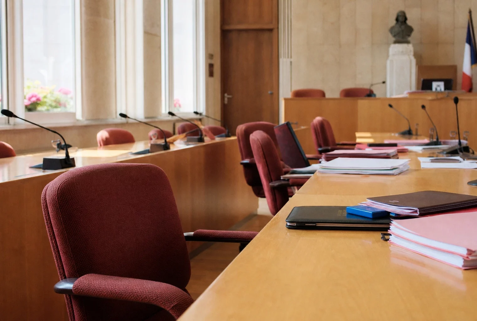 Salle municipale française vue en oblique avec chaises vides, micros et dossiers flous, ambiance politique sobre et claire.
