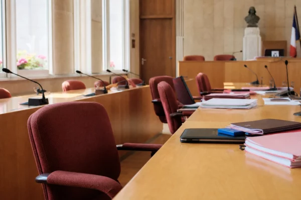 Salle municipale française vue en oblique avec chaises vides, micros et dossiers flous, ambiance politique sobre et claire.