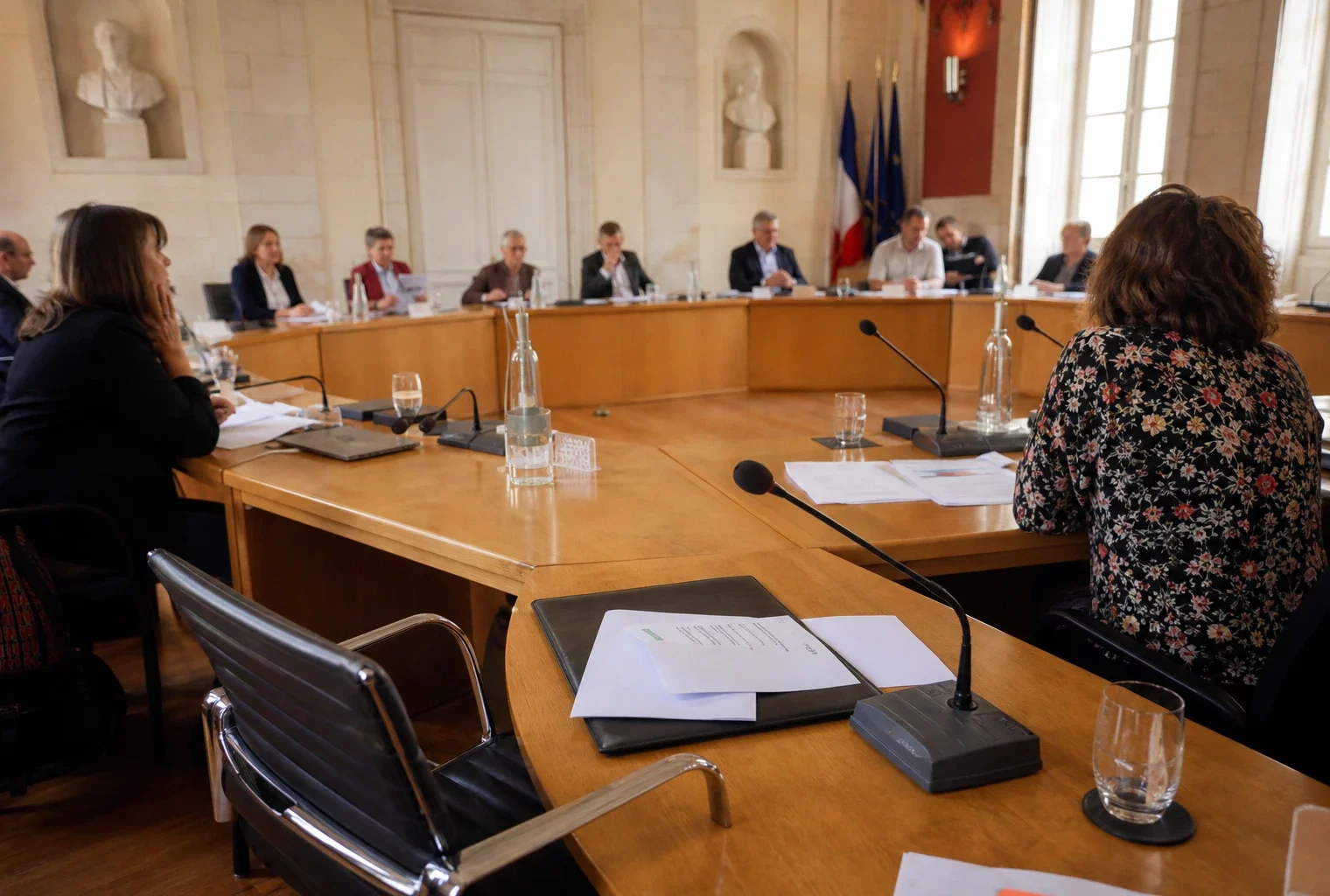 Salle municipale claire avec chaise vide, micros et dossiers sur une table de conseil, scène politique française réaliste.