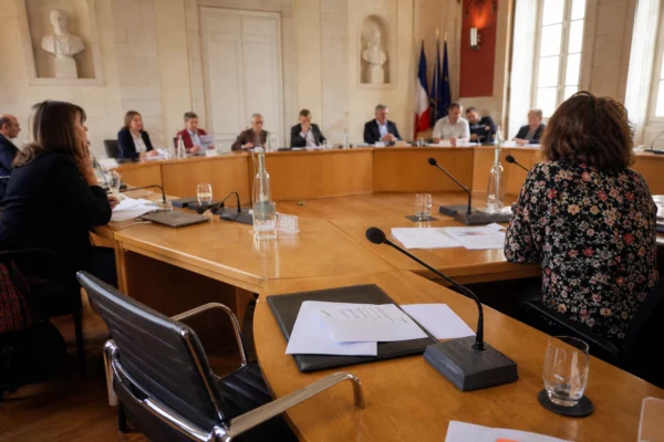 Salle municipale claire avec chaise vide, micros et dossiers sur une table de conseil, scène politique française réaliste.