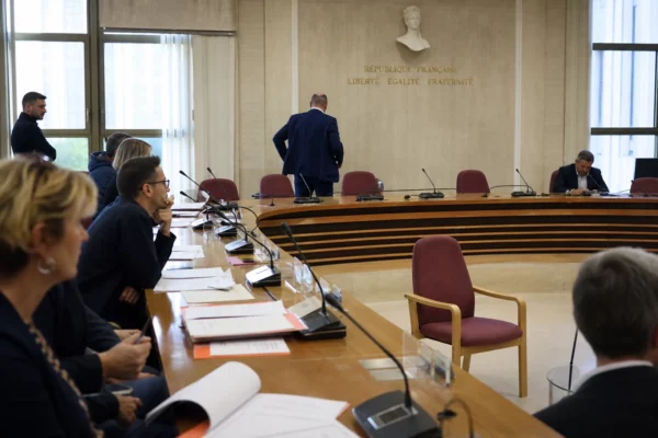 Salle de conseil municipal en France avec chaise vide, micros et dossiers flous sous une lumière naturelle claire.