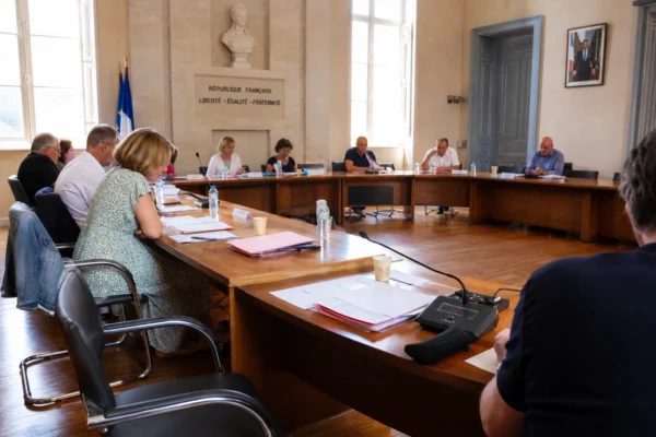 Salle municipale en Gironde avec micros, dossiers flous et chaise vide, dans une ambiance de réunion locale calme.