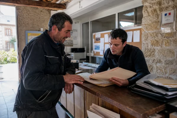 Dans une coopérative agricole de village, un farmer et une employée examinent des dossiers sur un comptoir en bois.