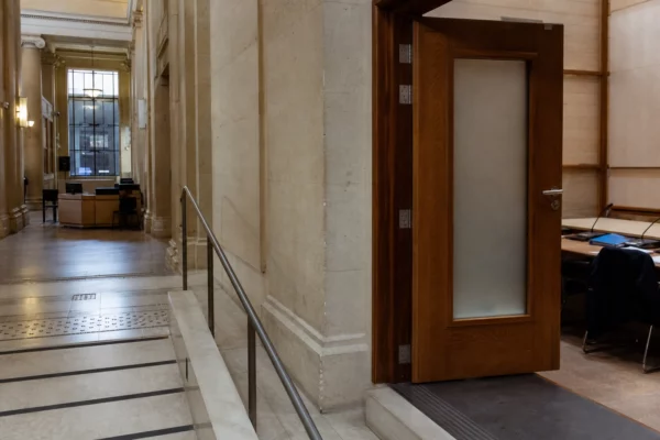 Couloir clair d’un bâtiment institutionnel français menant à une salle d’audition, ambiance sobre et documentaire.