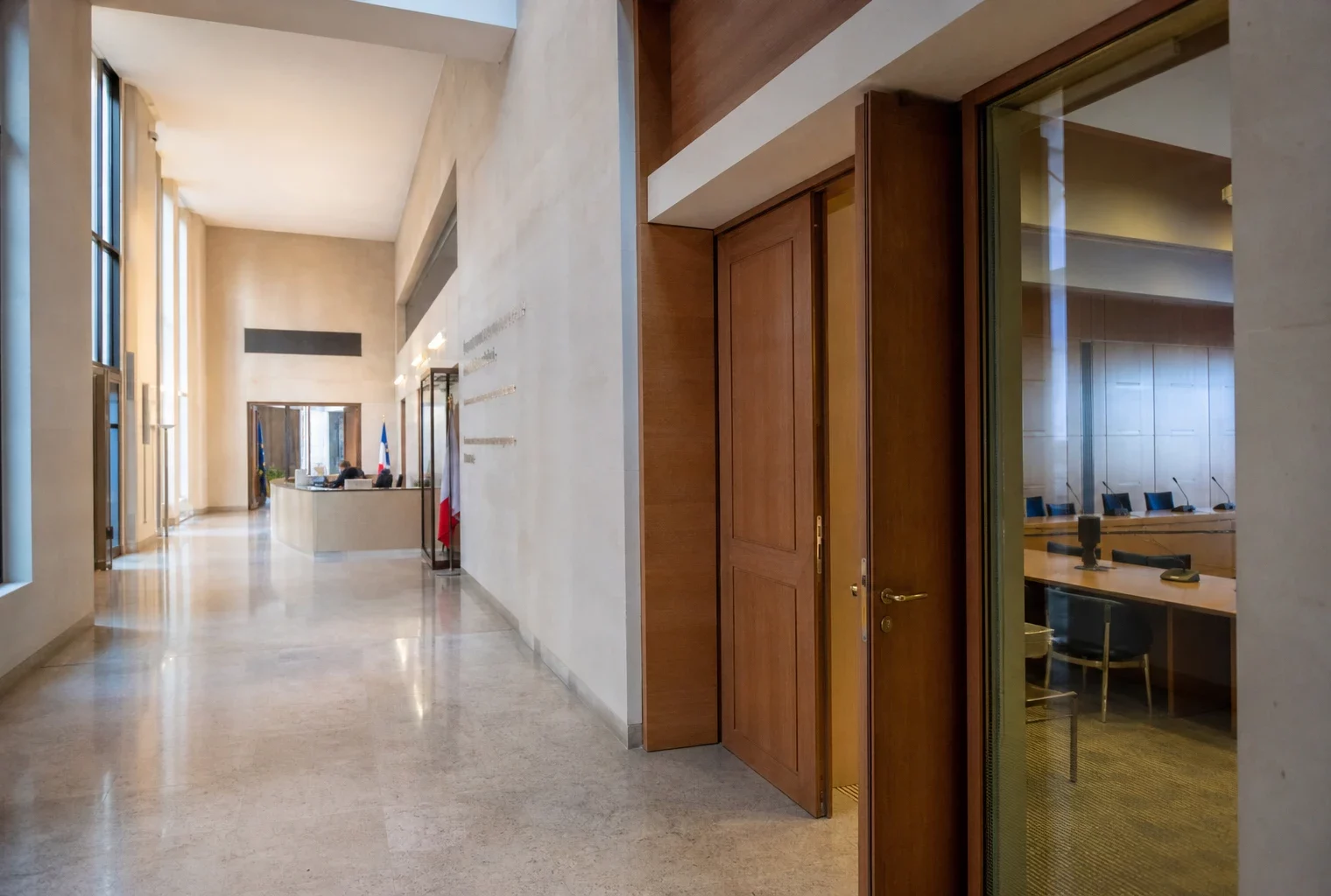 Couloir lumineux d’une institution publique française, porte entrouverte et salle d’audition discrète en arrière-plan.