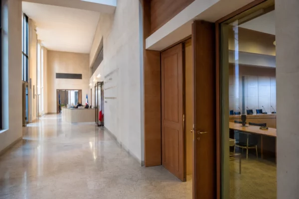 Couloir lumineux d’une institution publique française, porte entrouverte et salle d’audition discrète en arrière-plan.