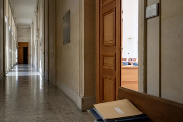 Couloir clair d’un bâtiment institutionnel français avec porte entrouverte vers une salle d’audition
