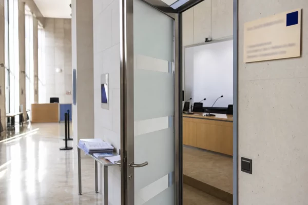 Couloir clair d’un bâtiment institutionnel français menant à une salle d’audition sobre et vide.