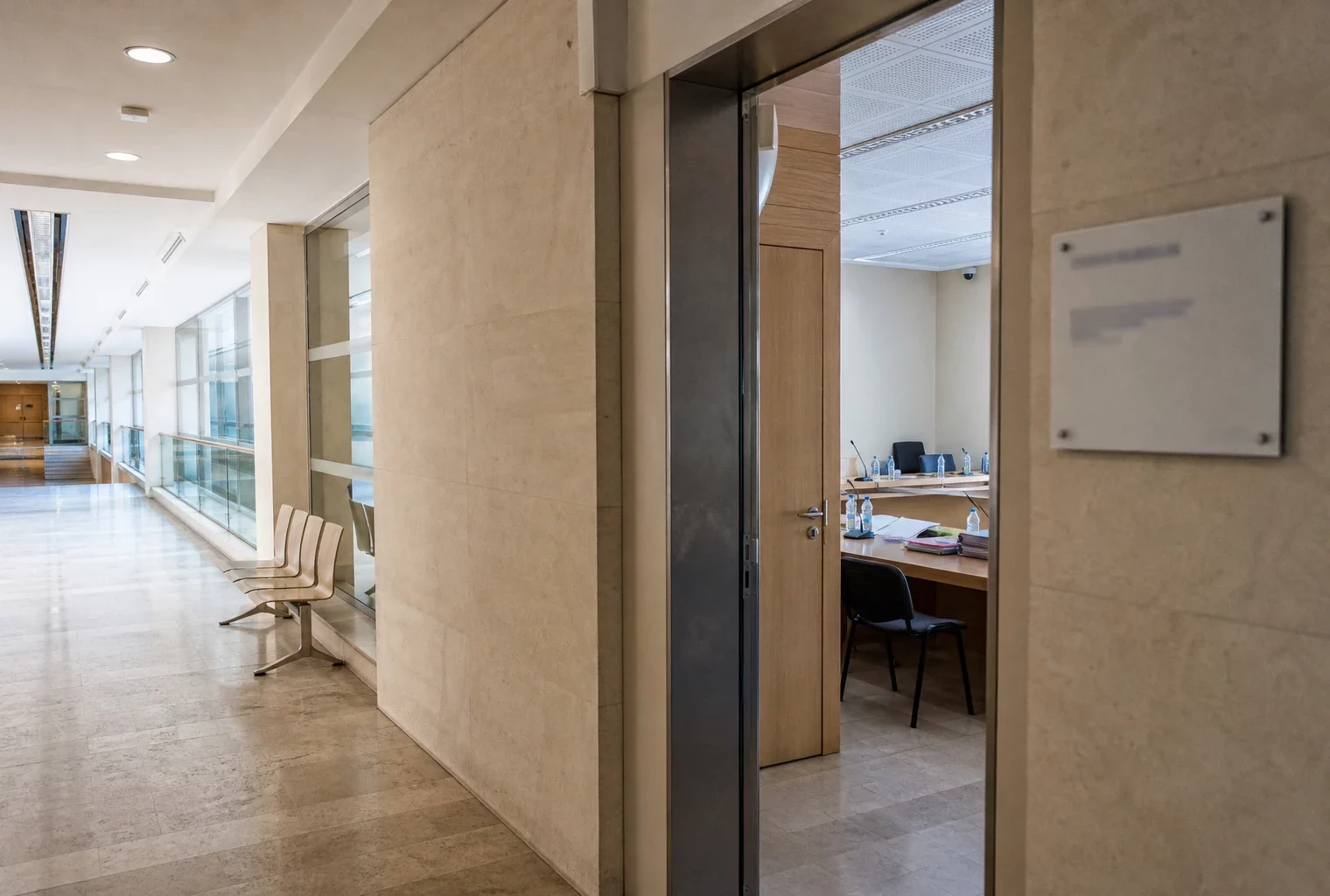 Couloir lumineux d’un bâtiment institutionnel avec une salle d’audition visible au fond, ambiance de reportage politique.