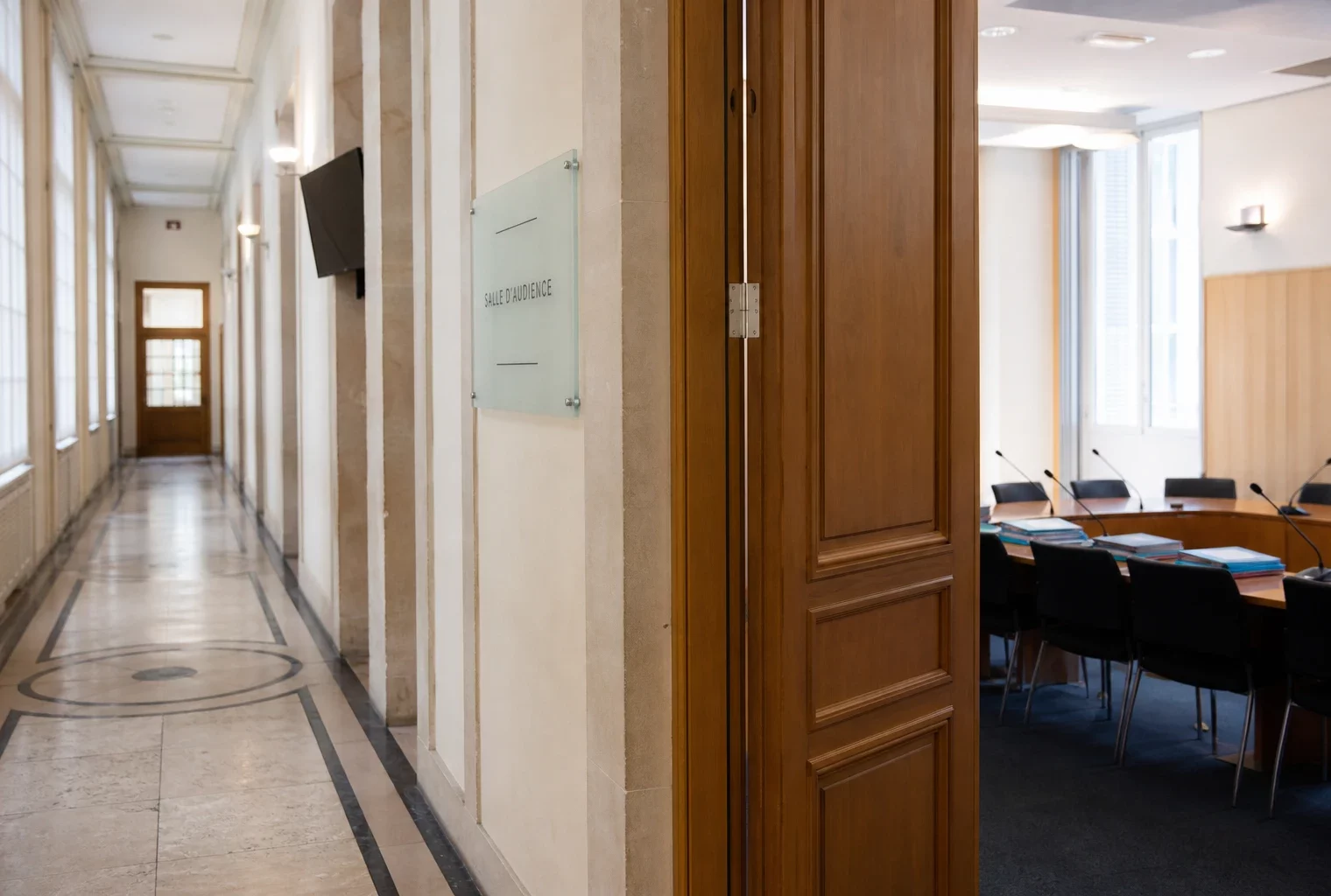 Couloir clair d’un lieu institutionnel français avec salle d’audition visible en arrière-plan