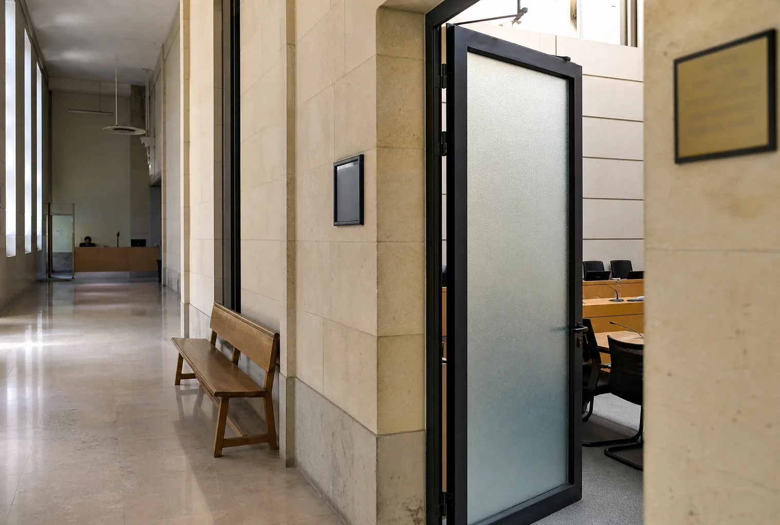 Couloir clair d’une institution publique française menant à une salle d’audition, avec porte sobre et lumière naturelle.