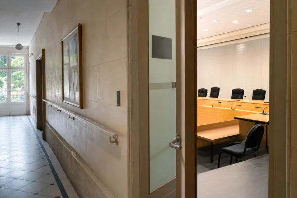 Couloir clair d’une institution publique française avec porte entrouverte sur une salle d’audition vide