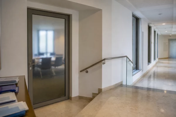Couloir clair d’une institution publique française, porte sobre et lumière naturelle, vue d’ensemble en photo de presse.