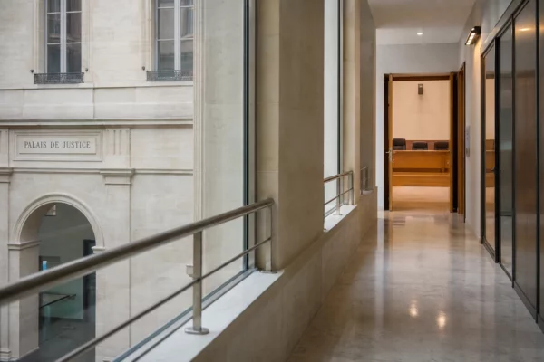 Couloir clair d’un bâtiment institutionnel français avec salle d’audition visible au fond.