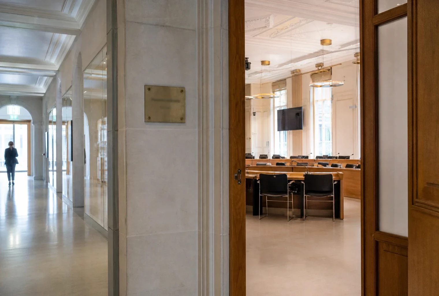 Couloir lumineux d’un bâtiment institutionnel français avec porte entrouverte vers une salle d’audition vide.