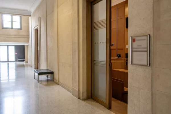 Couloir clair d’un bâtiment judiciaire français, porte sobre et salle d’audition en perspective oblique.
