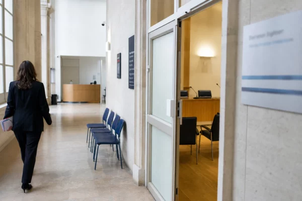 Couloir lumineux d’un bâtiment institutionnel français, avec porte sobre et salle d’audition en arrière-plan.