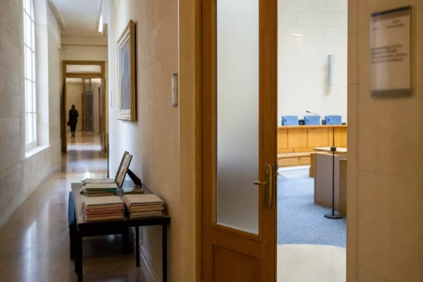 Couloir clair d’une institution française, porte entrouverte vers une salle d’audition vide, ambiance officielle et sobre.