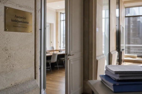 Couloir clair d’une autorité indépendante avec porte entrouverte sur une salle d’audition vide