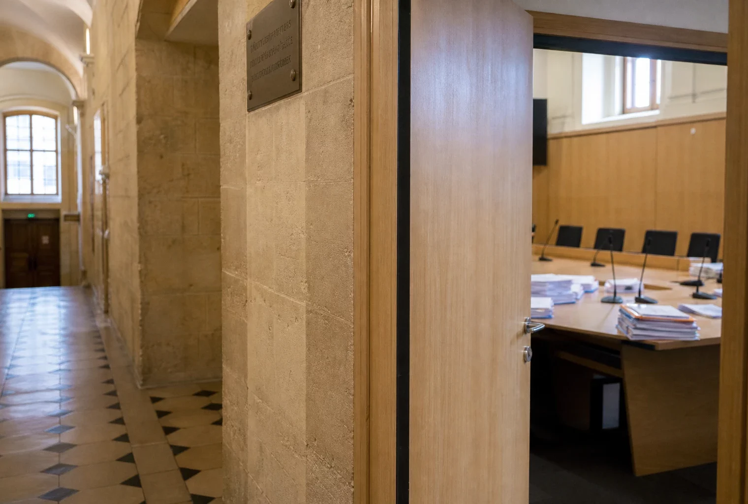 Couloir clair d’une institution française avec salle d’audition vide, micros et dossiers anonymes, en lumière naturelle.