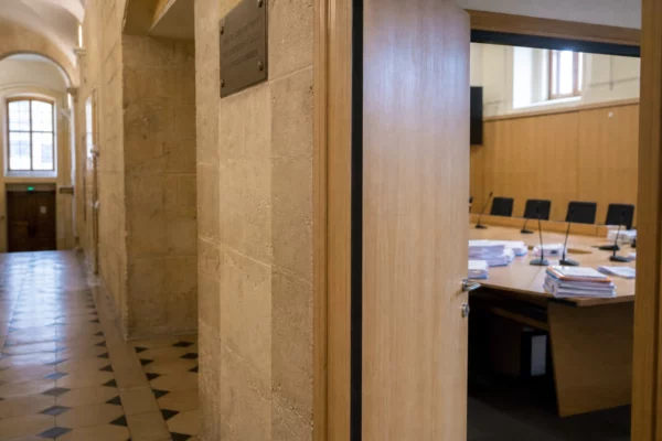 Couloir clair d’une institution française avec salle d’audition vide, micros et dossiers anonymes, en lumière naturelle.