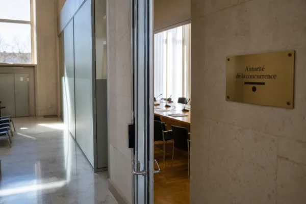 Couloir lumineux d’un bâtiment institutionnel français avec salle d’audition floue et dossiers sur une table