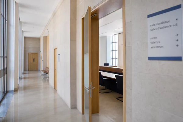 Couloir lumineux d’un bâtiment institutionnel français avec porte entrouverte sur une salle d’audition vide