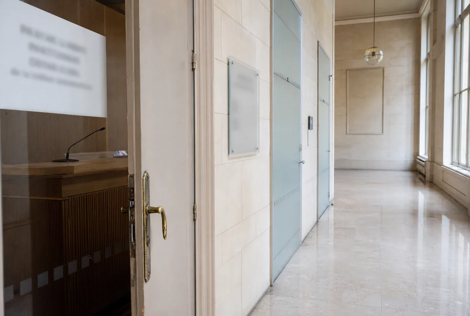 Couloir lumineux d’un bâtiment institutionnel français avec porte d’audition entrouverte et plaques floues