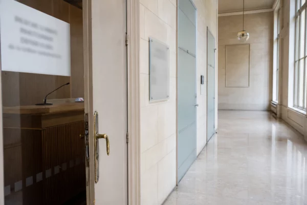 Couloir lumineux d’un bâtiment institutionnel français avec porte d’audition entrouverte et plaques floues