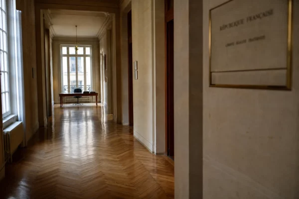 Couloir lumineux d’un siège politique français vide, avec parquet, portes closes et dossiers flous sur une table.