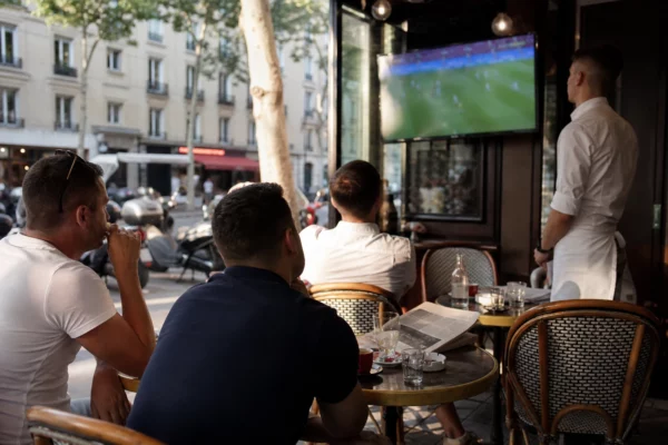 Terrasse de café française avec supporters regardant un match de football à la télévision, en ambiance de reportage.
