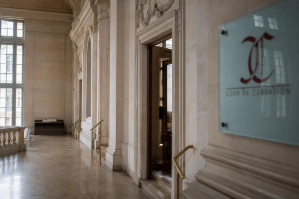Hall institutionnel vide d’un palais de justice parisien, en lumière naturelle claire et vue oblique.