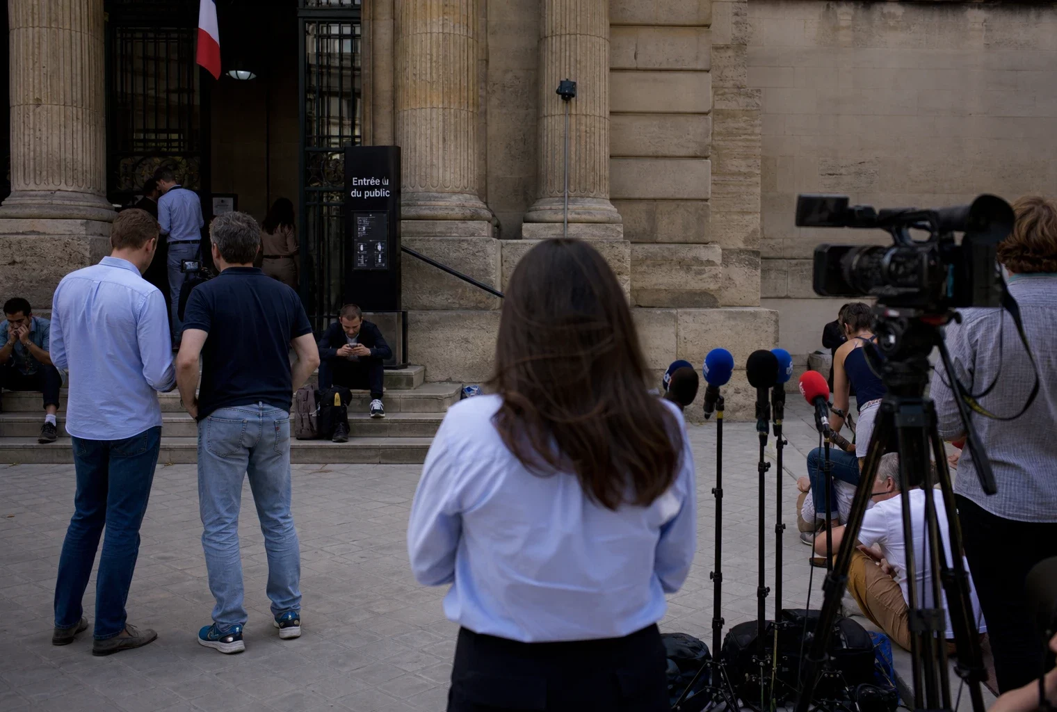 Reportage devant un palais de justice parisien avec journalistes et passants dans une atmosphère calme avant une décision judiciaire.