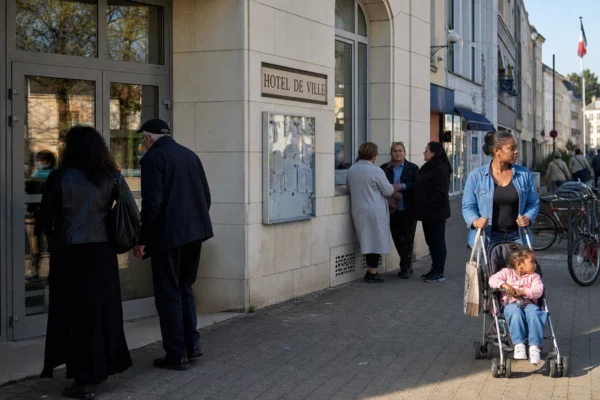 Des habitants traversent le centre de Creil devant la mairie, dans une scène urbaine claire et naturelle.