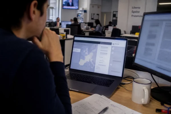 Vue de dos d’un journaliste devant un écran d’ordinateur avec interface abstraite, dans une rédaction française lumineuse.