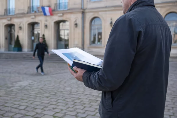 Un élu local de dos tient un dossier devant la mairie de Saint-Avold, en lumière naturelle claire.